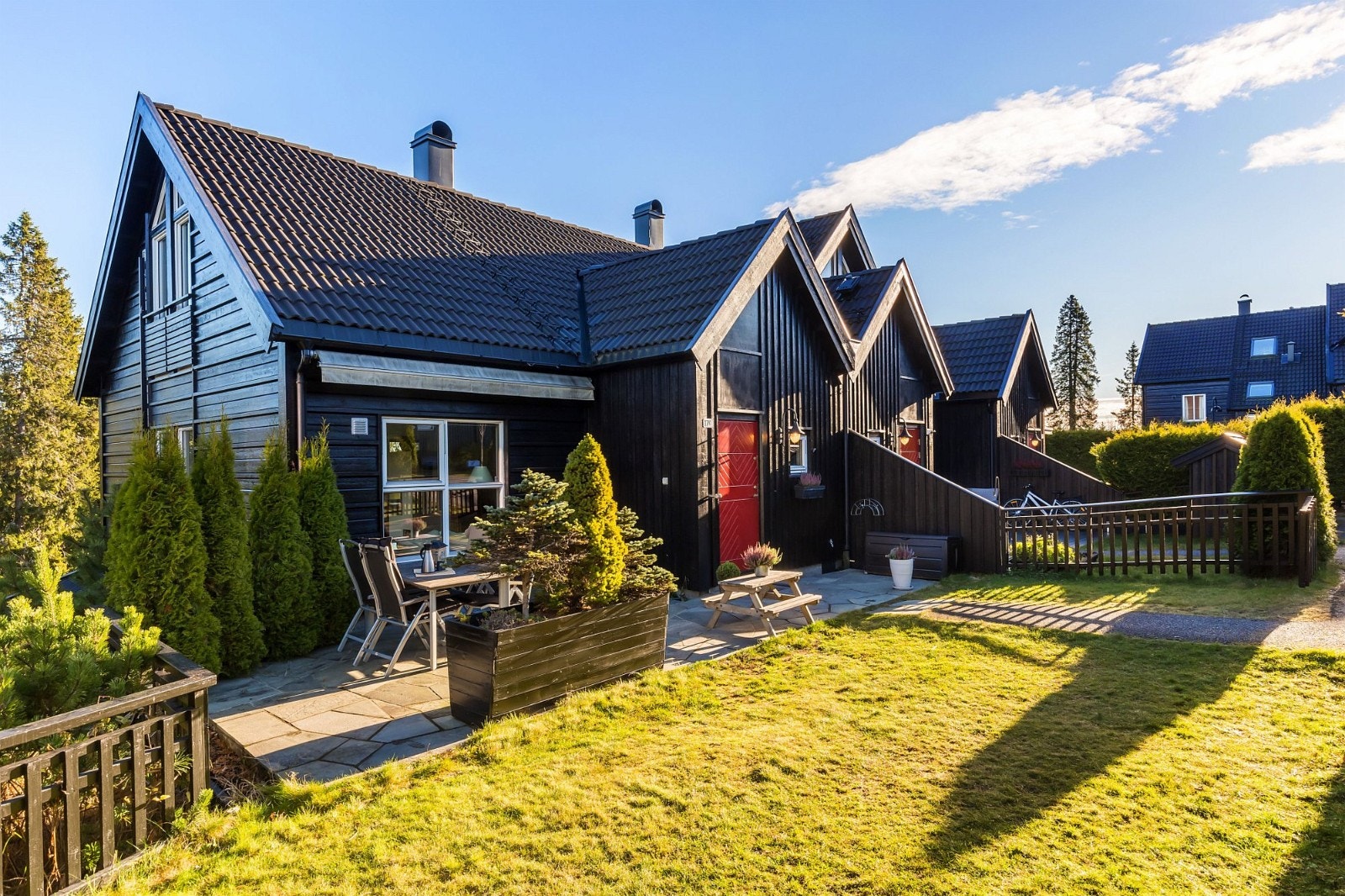 Her er et bilde av huset vårt og litt av naboens hus og så kan man se et hus til lenger bak. På plenen kan man spille fotball og de voksne pleier a drikke kaffe borte ved stolene. Galleribilde