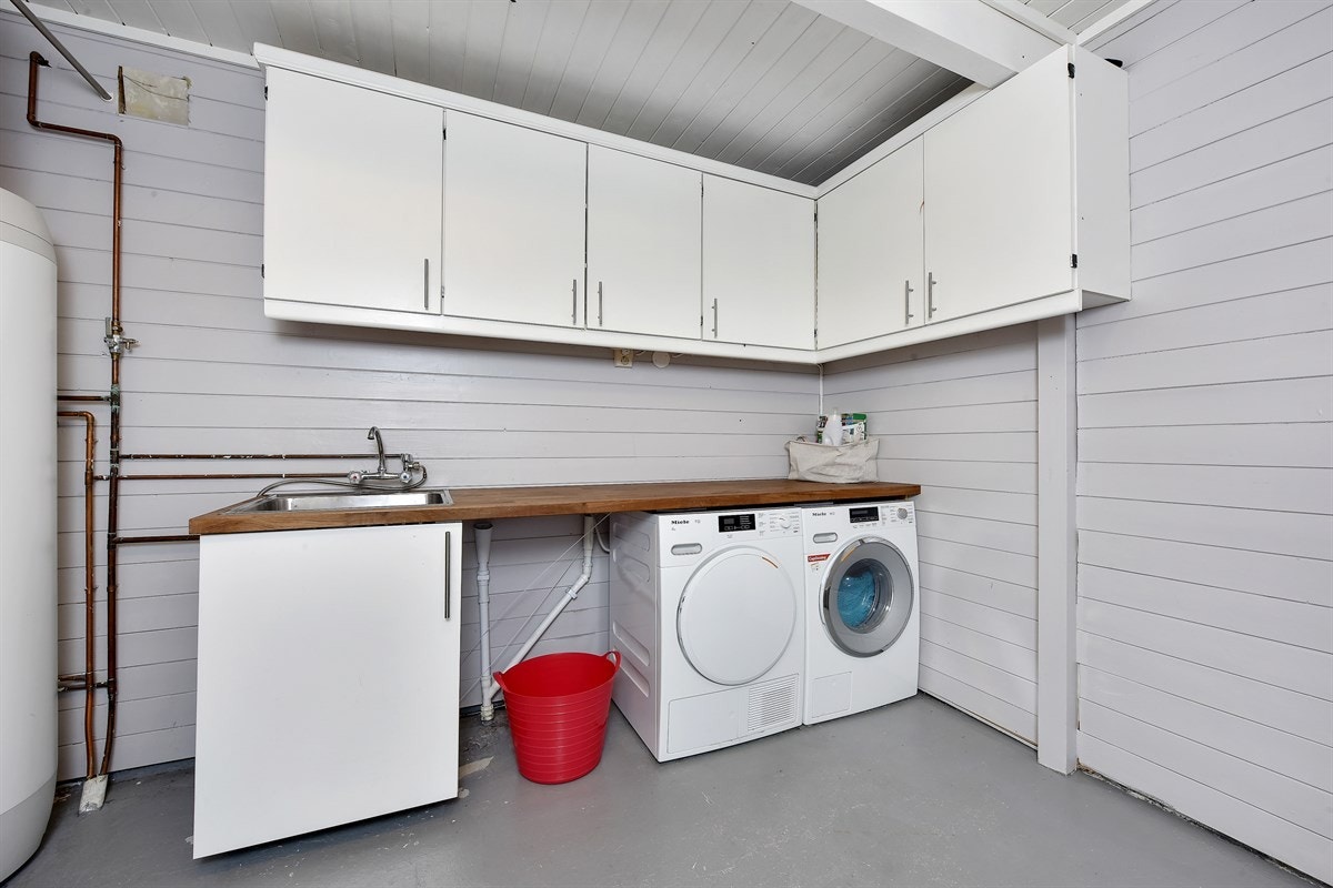 Vaskerom i første etasje er utstyrt med benkeplate, utslagsvask i metall, underskap, overskap og opplegg for vaskemaskin og tørketrommel. Rommet har malte vegger, malt panel i tak og malt murpuss på gulv. Galleribilde