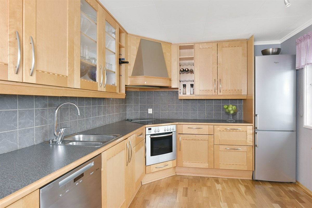 Innredningen har profilerte fronter, laminert benkeplate, dobbel oppvaskkum, vitrineskap, vinhylle, benkebelysning og fliser over benk. Galleribilde