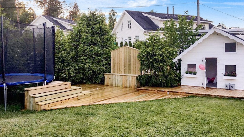 Dukkehus i hagen med nedfelt sandkasse i plattingen og trapp opp til trampolinen Galleribilde