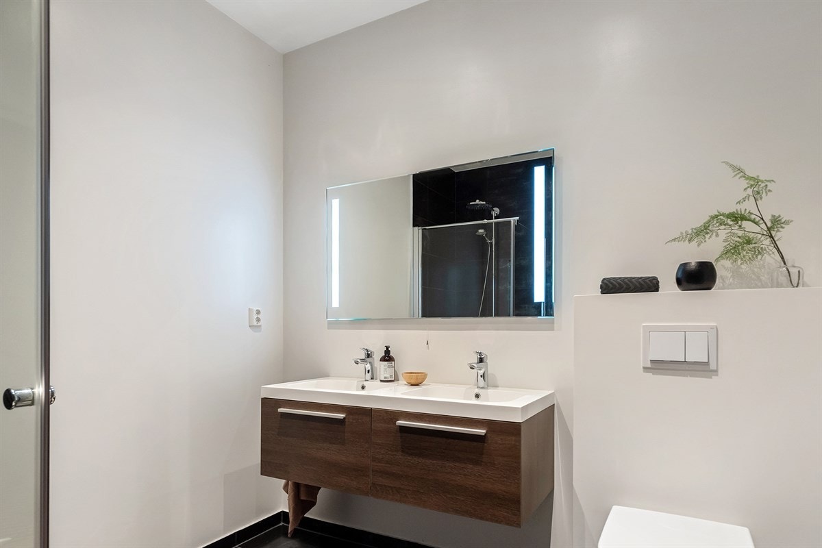 Detaljer som delikate flisvalg, glassvegger i dusjsone, speil med integrert belysning, moderne baderomsinnredning, vegghengt toalett, downlights og varmekabler Galleribilde