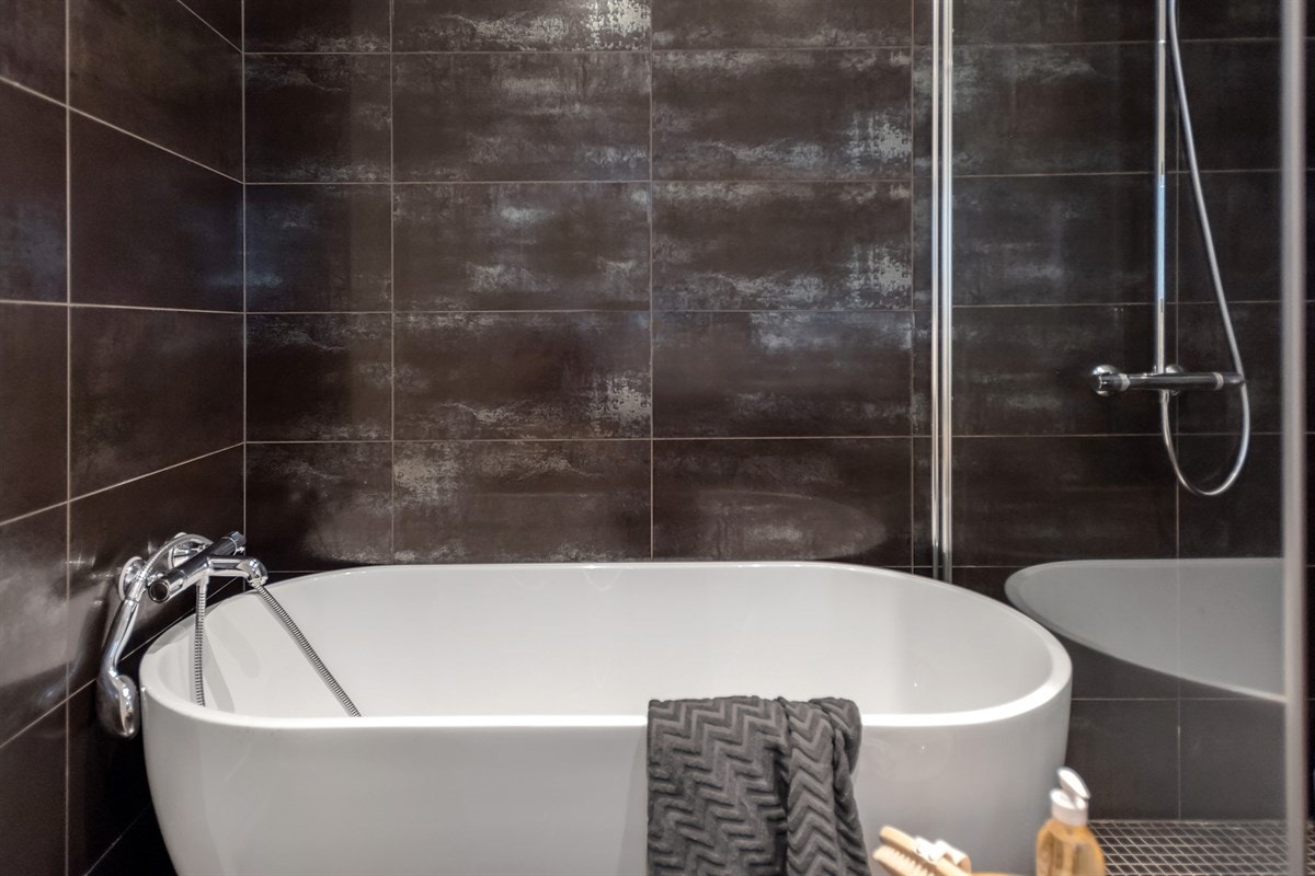 Detaljer som delikate flisvalg, glassvegger i dusjsone, speil med integrert belysning, moderne baderomsinnredning, vegghengt toalett, downlights og varmekabler Galleribilde