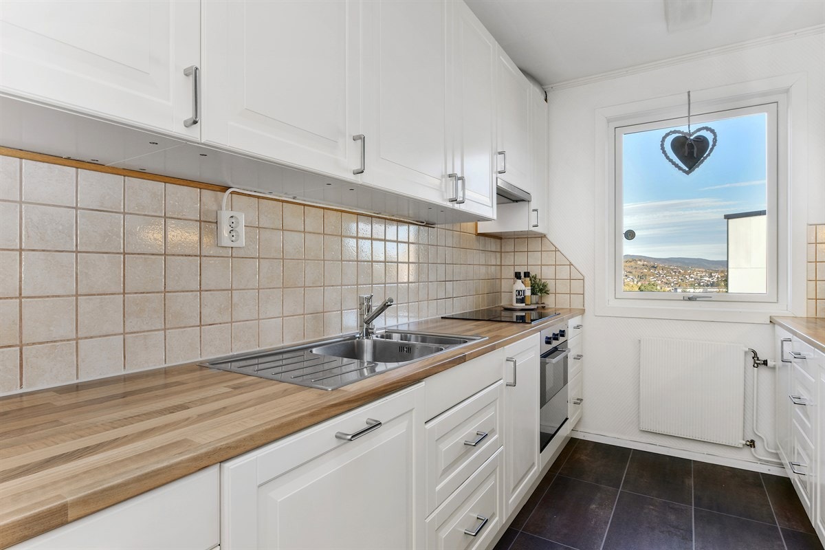 Innredningen har hvite profilfronter, vitrineskap med frostet glass, laminatbenkeplater i imitert tre, og nedfelt beslag med vaske- og skyllekum. Galleribilde