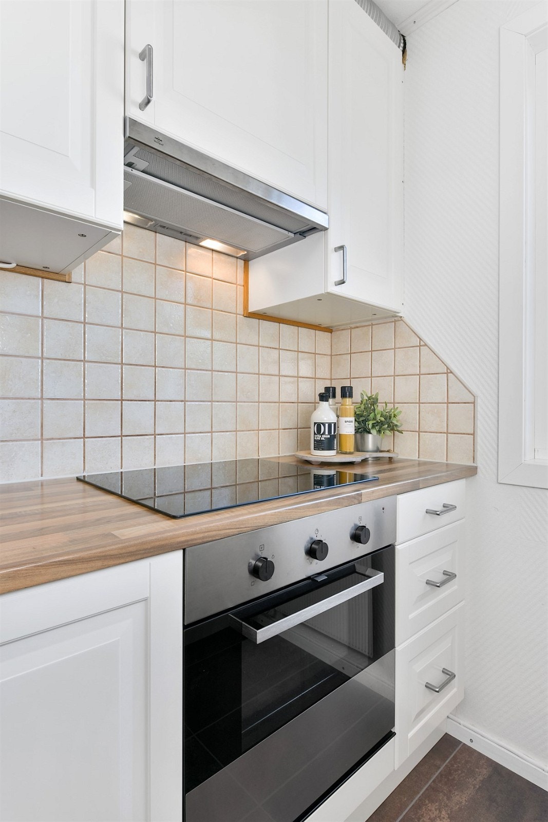 Videre har kjøkkenet integrert stekeovn, keramisk topp, oppvaskmaskin, ventilator og plass for kjøleskap. Rommet har grått, flismønstret gulvbelegg. Galleribilde