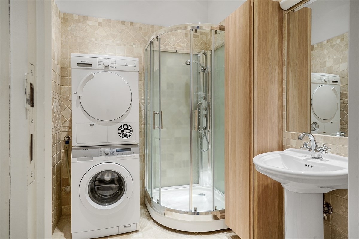 Leilighet 1. etasje. Dusjbadet har samme type fliser, gulvvarme og downlights. Rommet har søyleservant, speil med overlys, dusjkabinett og toalett. Dette badet har opplegg for vaskesøyle. Galleribilde