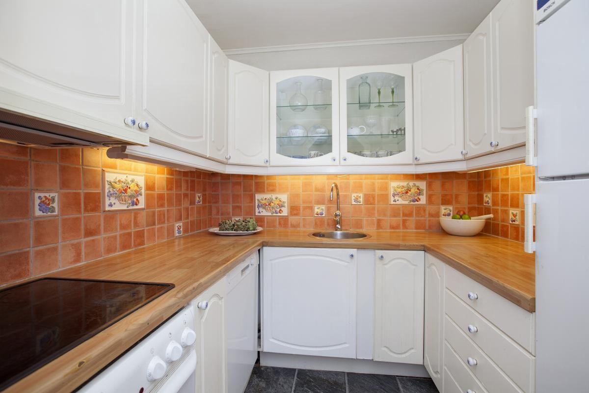 Hvit og profilert kjøkkeninnredning av eldre dato. Laminat benkeplate med nedfelt vask. Galleribilde