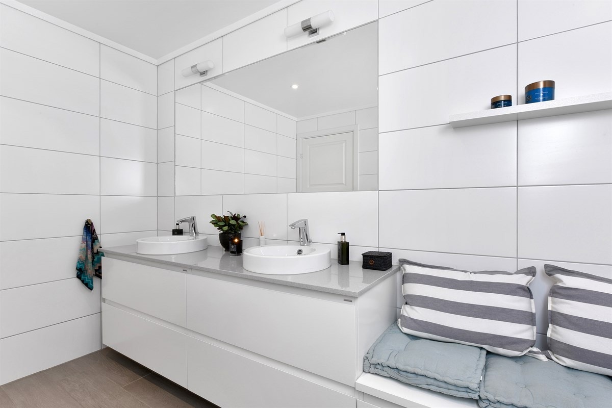 Innredningen består av to toppmonterte servanter på en benkeplate av stein, med underskuffer og en praktisk sidebenk. Galleribilde