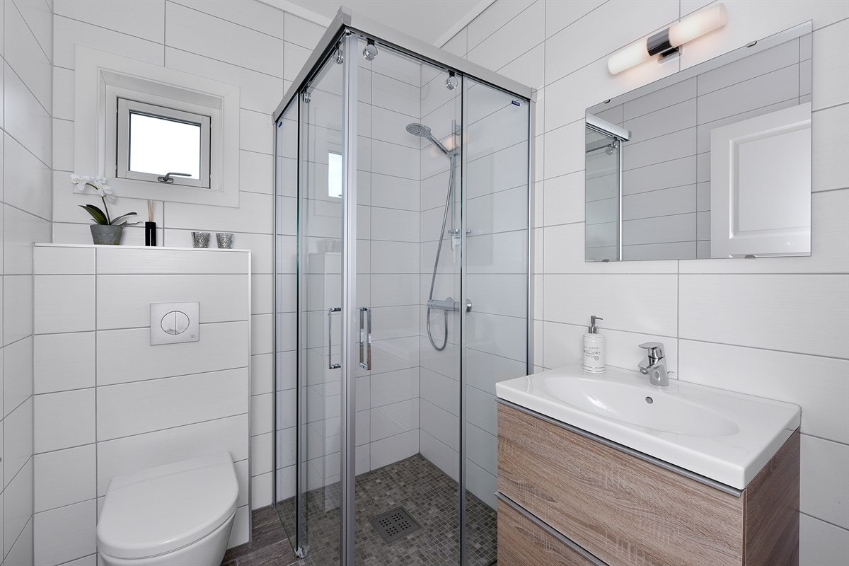 Badet i første etasje har også mørke fliser på gulv og lyse fliser på veggene, samt gulvvarme, veggmontert toalett og et dusjhjørne med innfellbare glassdører. Galleribilde