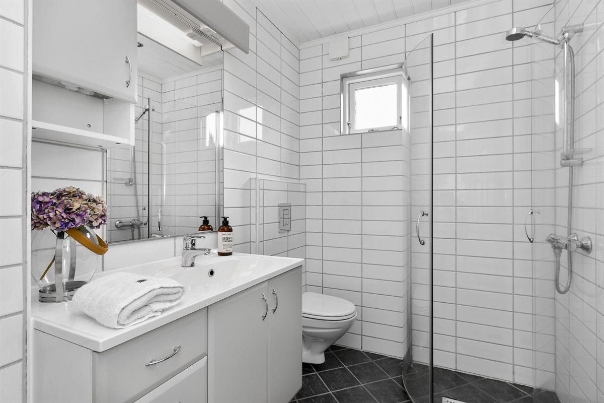 Badet ligger i første etasje og er fremstår som velholdt og pent med hvite fliser på veggene, hvitt panel med downlights i himling og grå fliser på gulvet. Galleribilde