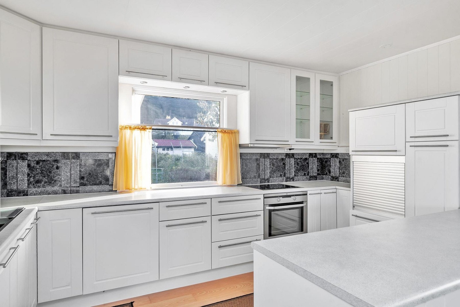 Integrert frys under benk, komfyr, kjøleskap og oppvaskmaskin. Fliser over benk. Galleribilde