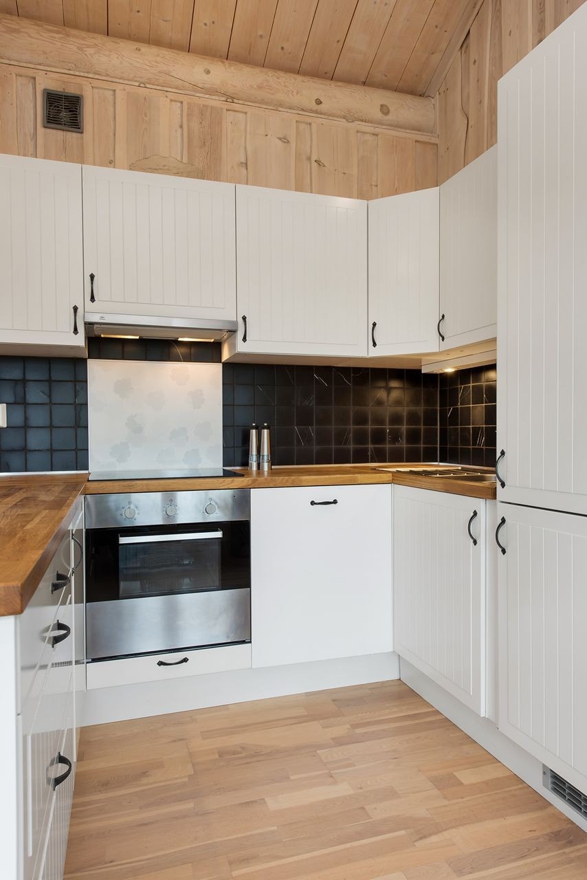 Praktisk innredet kjøkken, med integrerte hvitevarer. Fliser over benk. Galleribilde