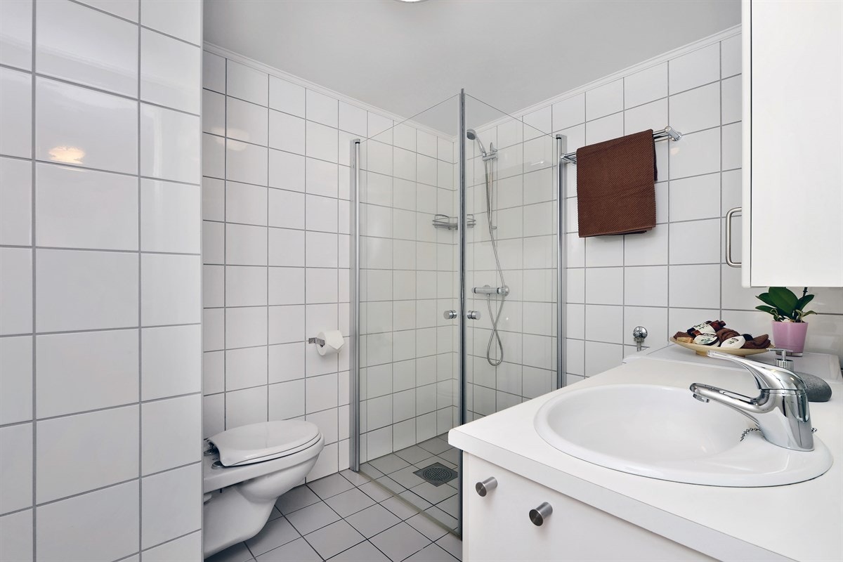 Badet er delikat med grå gulvfliser, hvite veggfliser og gulvvarme. Innredningen består av servant med underskap, veggskap og speil med belysning. Galleribilde