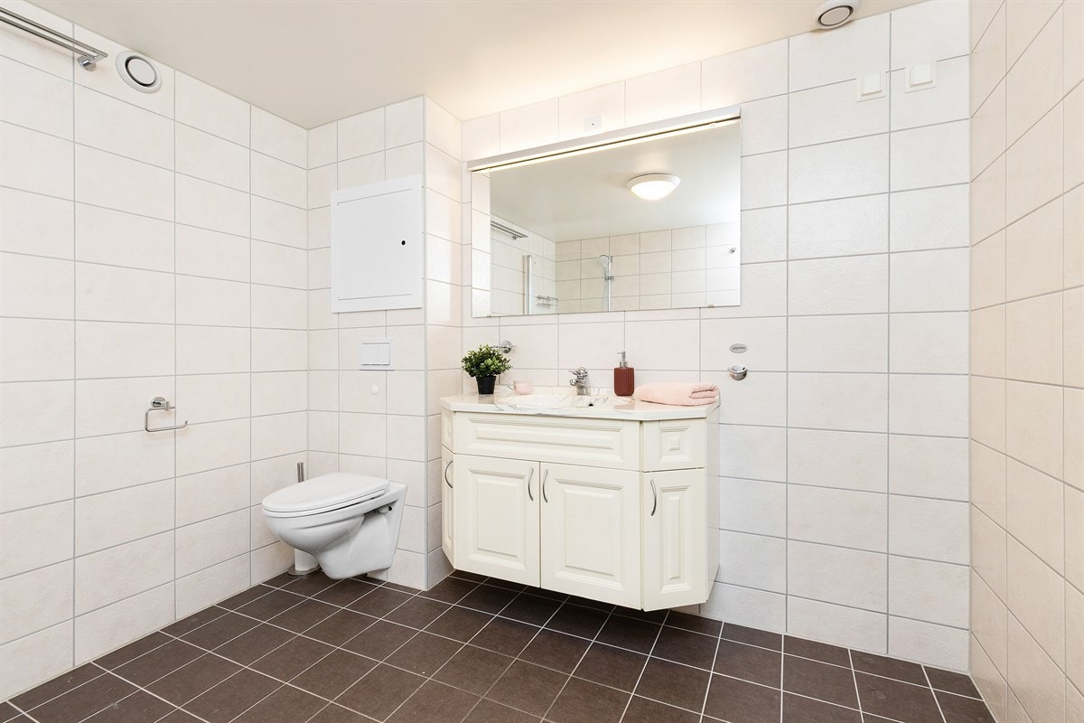 Badet har vegghengt toalett og opplegg for vaskemaskin, samt badekar med dusjløsning og glassvegg. Galleribilde