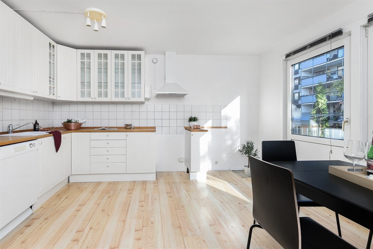 Et romslig kjøkken ligger i direkte tilknyttet stuen, med laminatgulv, hvitmalte vegger og plass til spisebord. Galleribilde