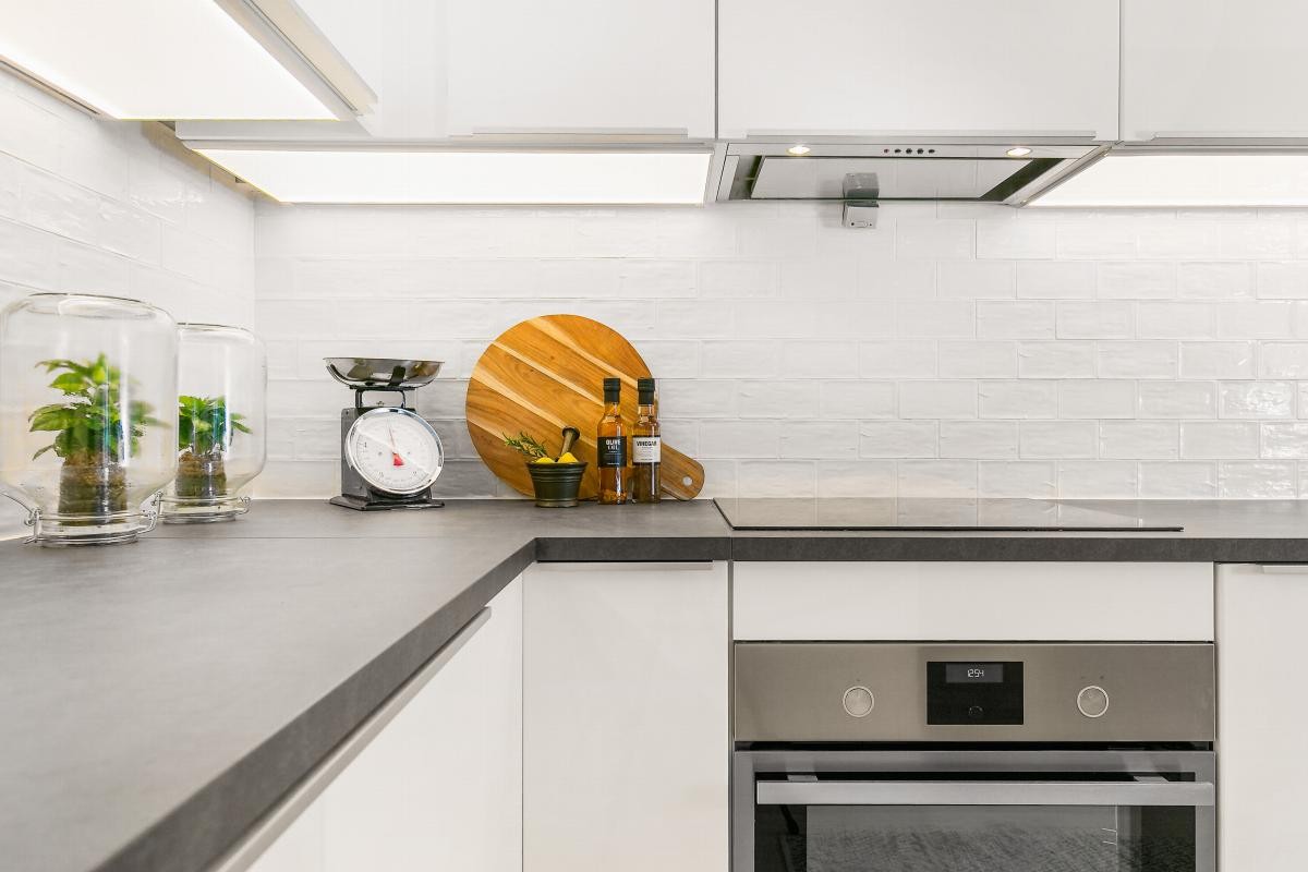 Innredningen har høyglansede, hvite fronter, sort benkeplate i laminat, og blanke, hvite fliser mellom benk og overskap. Galleribilde