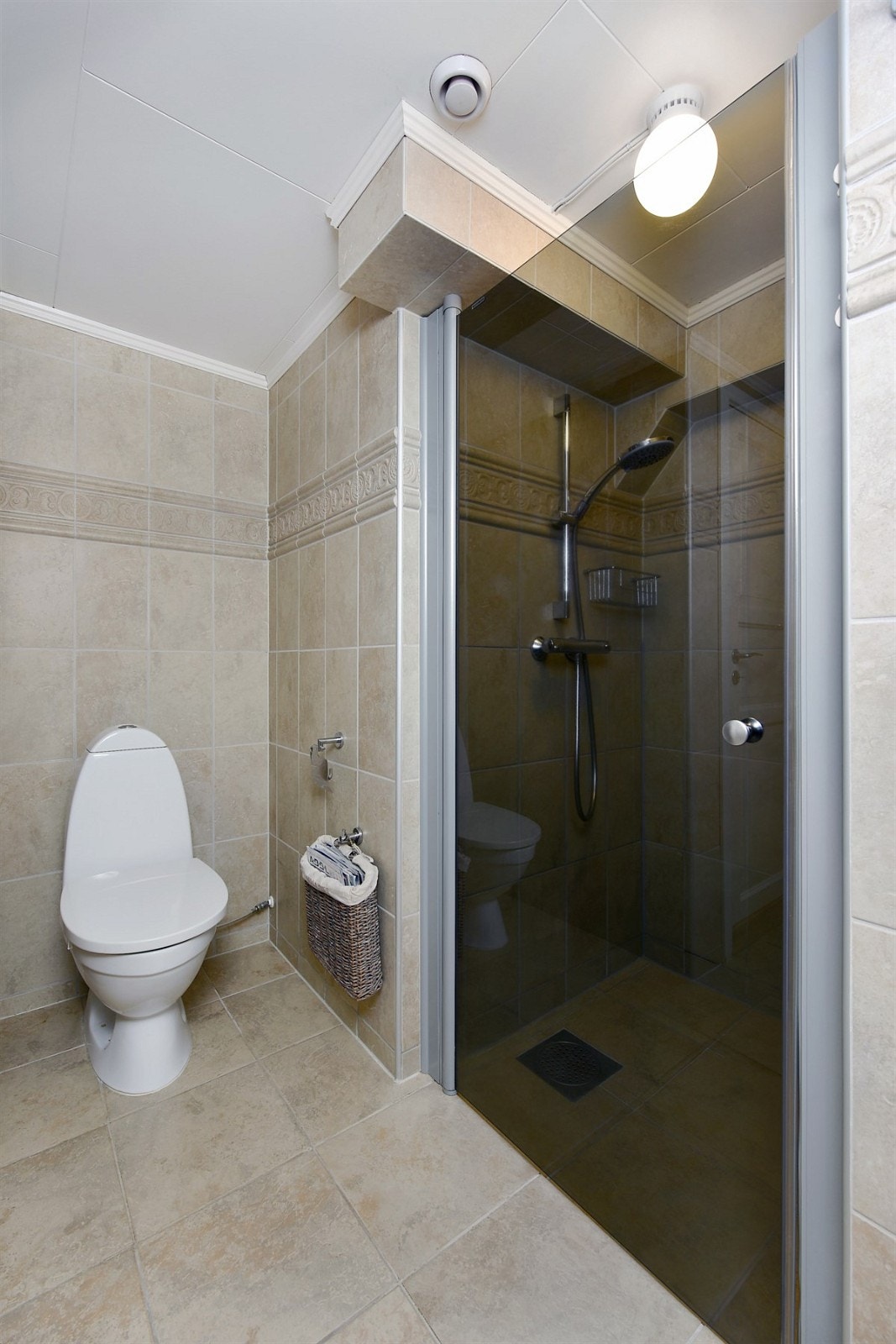 Rommet har innfliset badekar, dusjnisje med glassdør, gulvstående toalett og elektrisk håndkletørker. Galleribilde