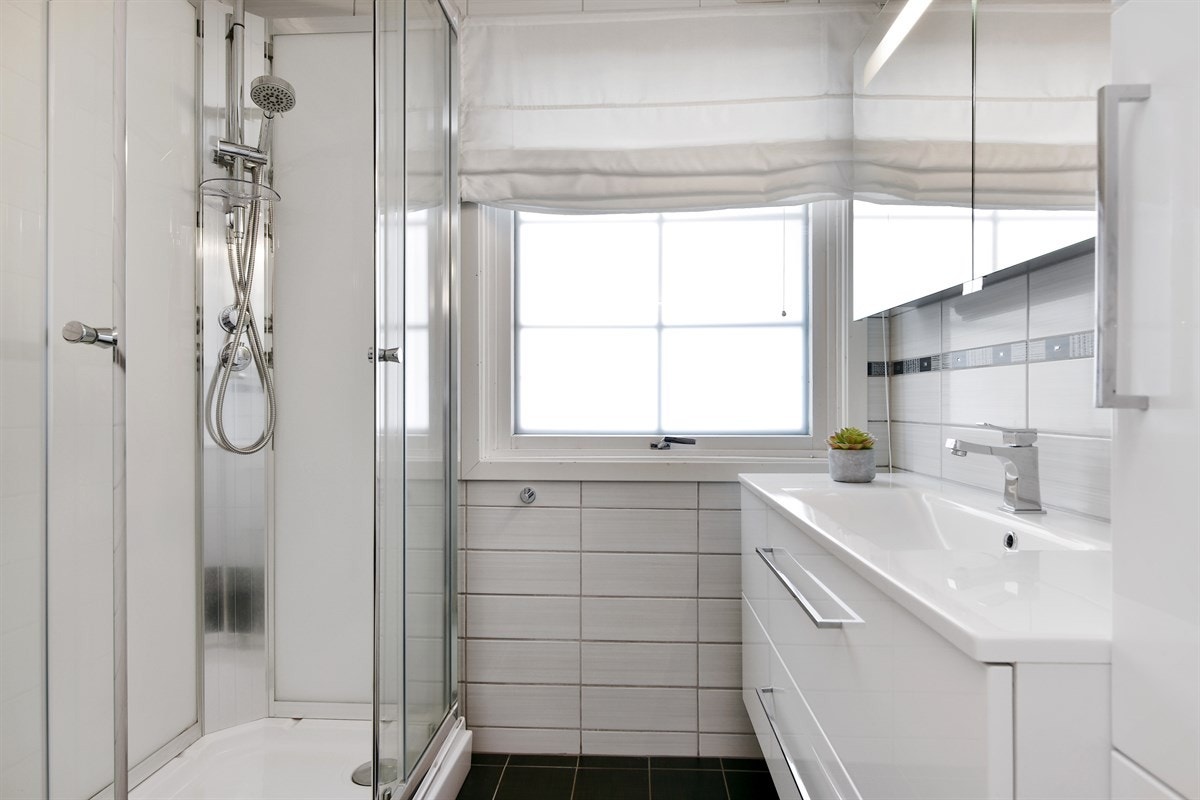 Badet i første etasje er lyst og delikat med hvite fliser på vegger og sorte fliser på gulv med varme. Galleribilde