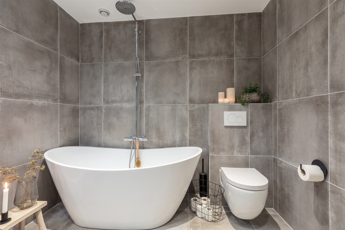 Begge badene har store, grå gulv- og veggfliser, gulvvarme og mekanisk avtrekk. Galleribilde