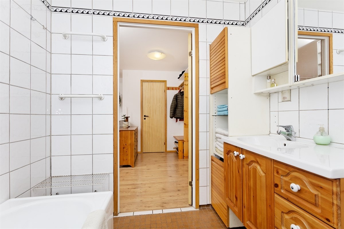 Badekar med dusj og forheng, toalett, servant med innredning og skap. Galleribilde