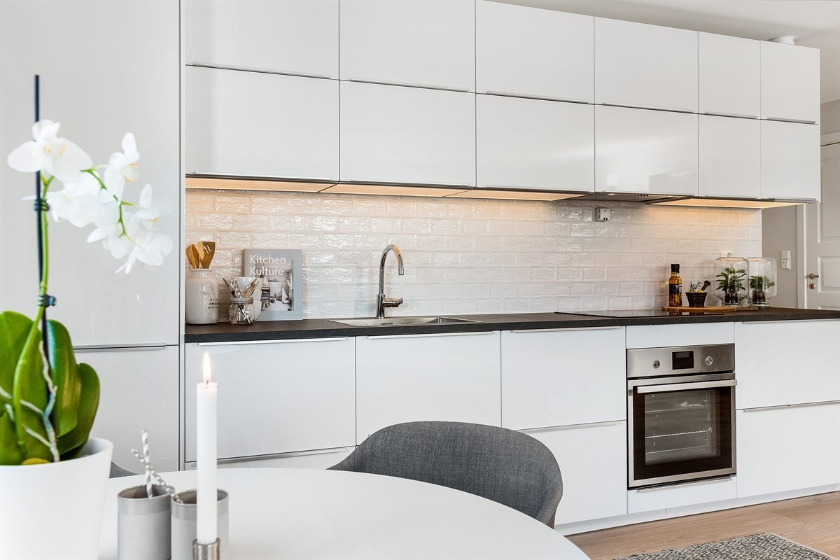 Innredningen har høyglansede, hvite fronter, sort benkeplate i laminat, og glassplate over benk og overskap. Galleribilde