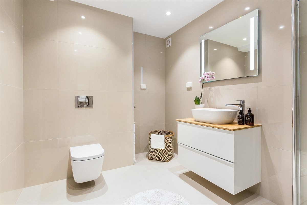 Innredningen består av en frittstående servant på en praktisk skuffeløsning med topplate i tre, et veggmontert toalett og opplegg for vaskemaskin. Galleribilde