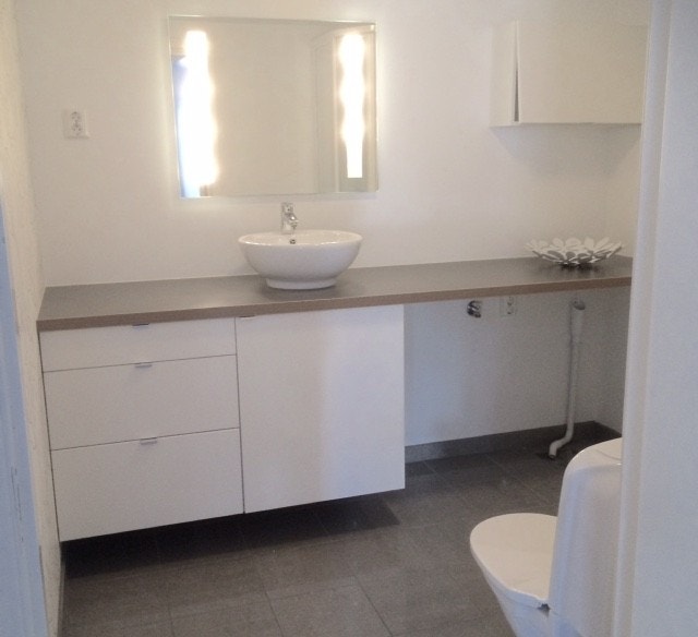 Lyst flislagt bad med opplegg for vaskemaskin og plass til kondens tørketrommel, dusjkabinett ag varmekabler i gulv. Nydelig effekttapet på ene veggen og speil med sminkelys. Galleribilde