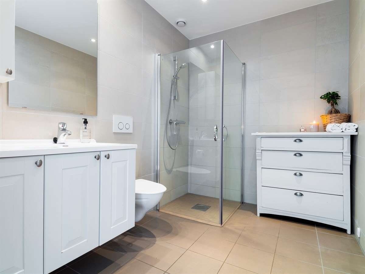 Badet i 2. etasje er utstyrt med varmekabler i gulv, dusjhjørne med innfellbare dusjdører, vegghengt toalett, hvit baderomsinnredning og downlights i tak. Galleribilde