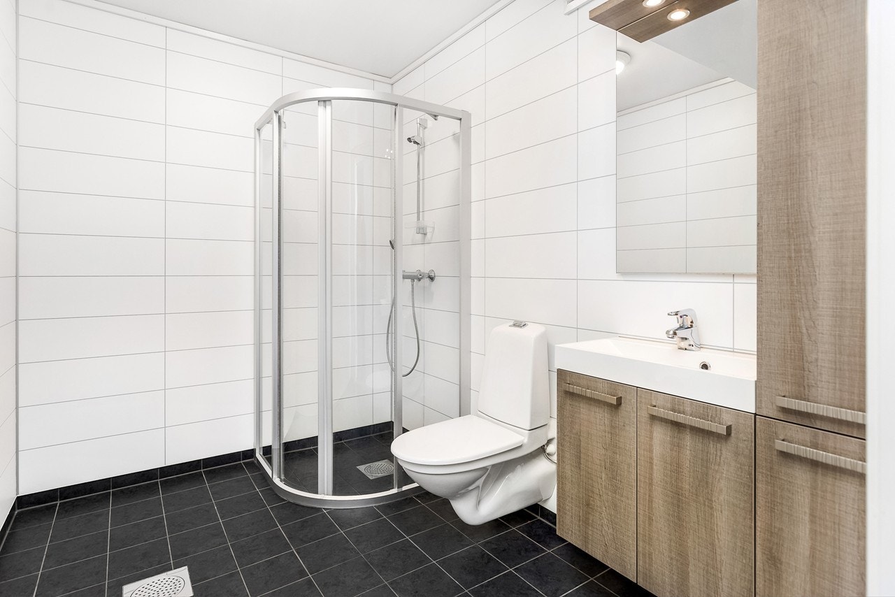 Boligen inneholder et delikat bad med sorte gulvfliser og hvite flisplater på veggene Galleribilde