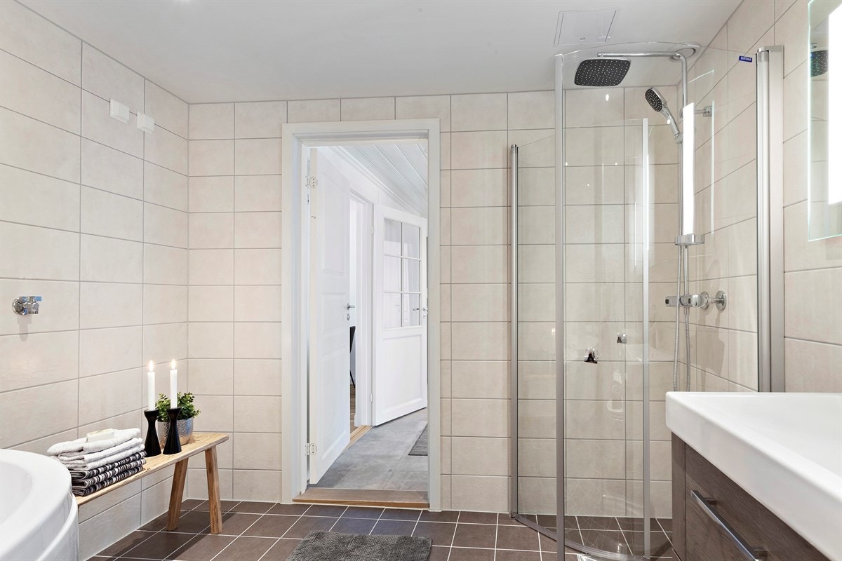 Badet er utstyrt med fliser på gulv og vegg, gulvvarme, downlights belysning, servant, servantmøblement, speil med integrert belysning og veggmontert toalett. Galleribilde