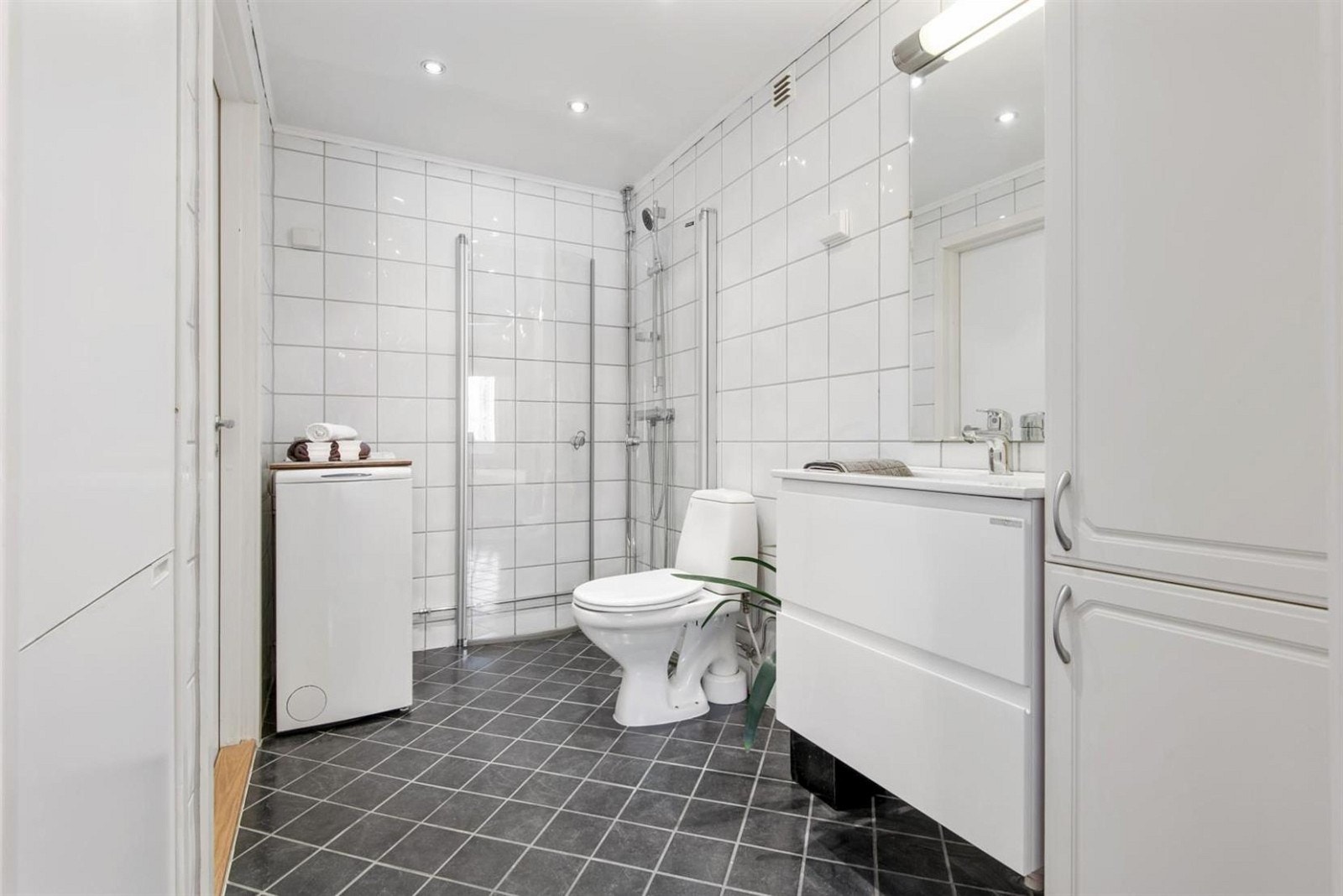 Pent, flislagt bad med dusjhjørne og opplegg for vaskemaskin. Galleribilde