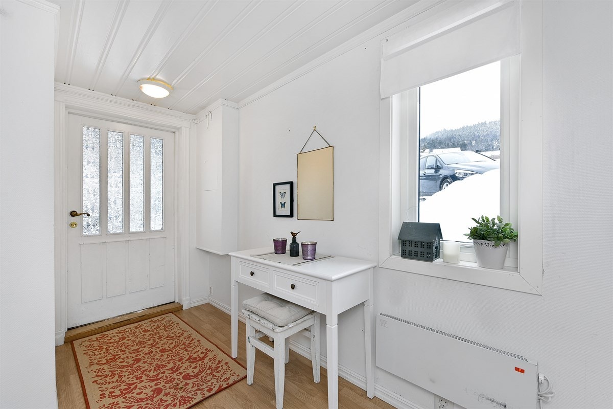 Trappen opp til entreen er gråmalt og det samme er entreens tregulv. Veggene er holdt med hvitmalt, liggende perlepanel og hvitmalt strietapet. Det lyse, tidsmessige fargevalget står godt i stil med øvrige rom i boligen. Galleribilde