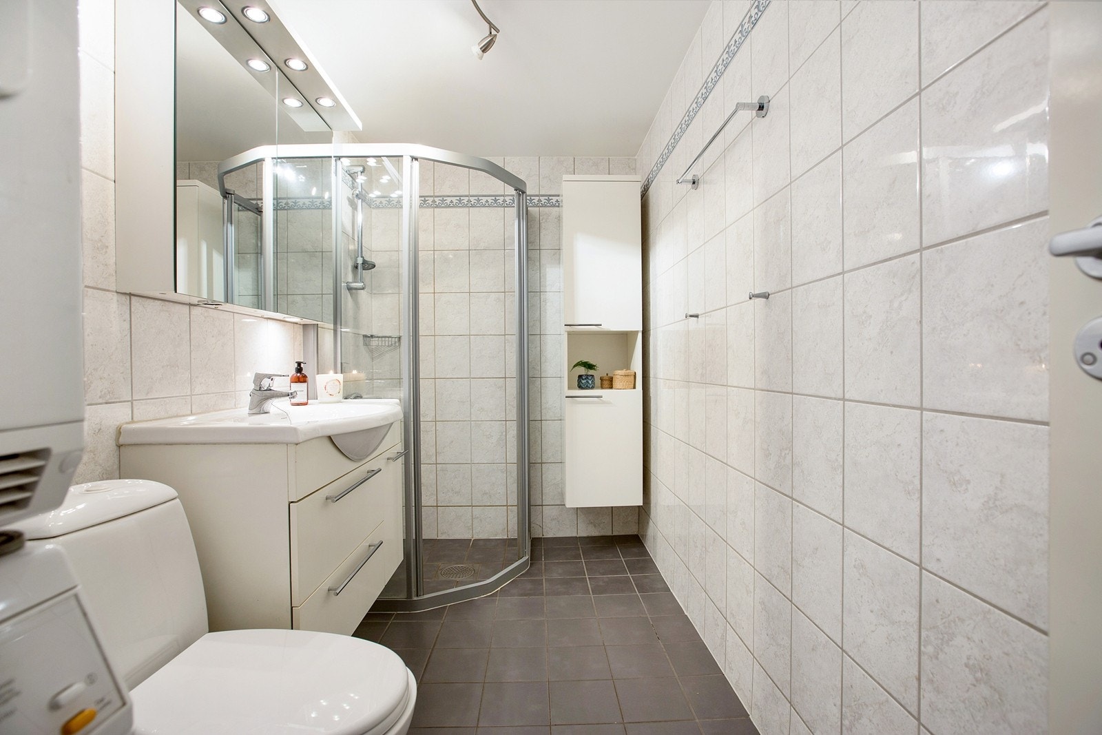 Flislagt baderom med praktisk dusjhjørne og vegghengt innredning. Opplegg for vaskemaskin og tørketrommel Galleribilde