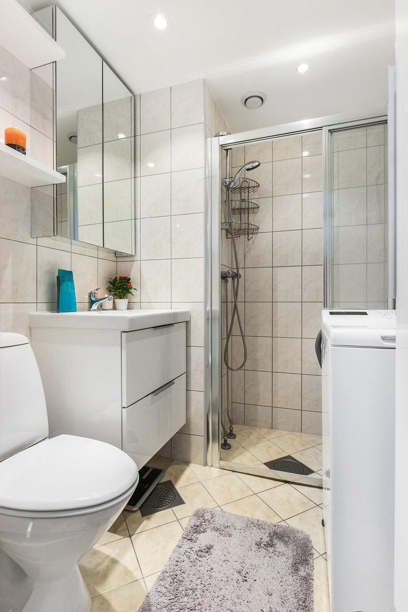 Pent flislagt badeværelse med servant på vegghengt servantskap, speilskap over, toalettt og dusjhjørne. Opplegg til vaskemaskin. Galleribilde