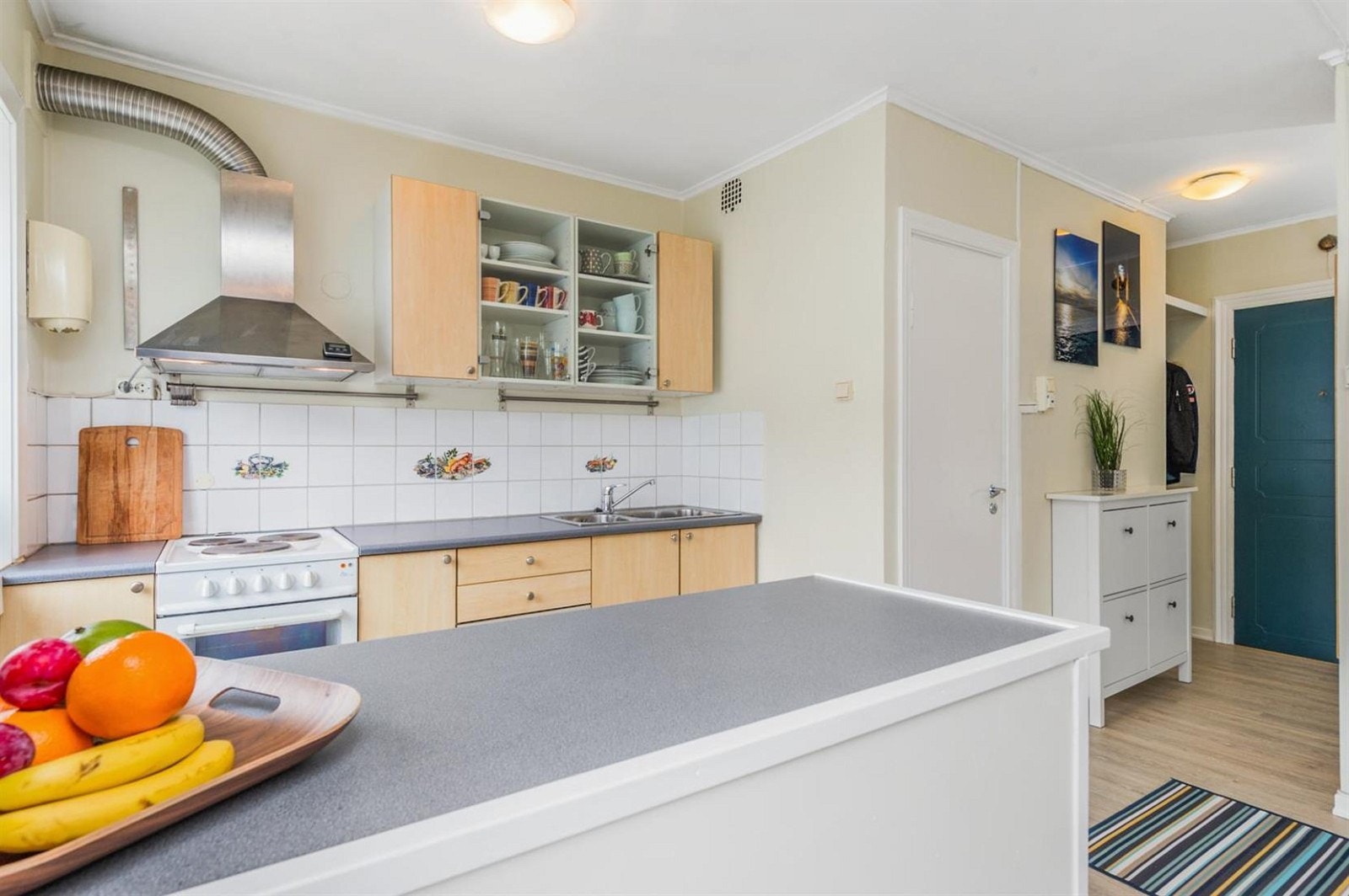 Enkelt kjøkken med øy, ventilator, kum i stål og komfyr. Galleribilde