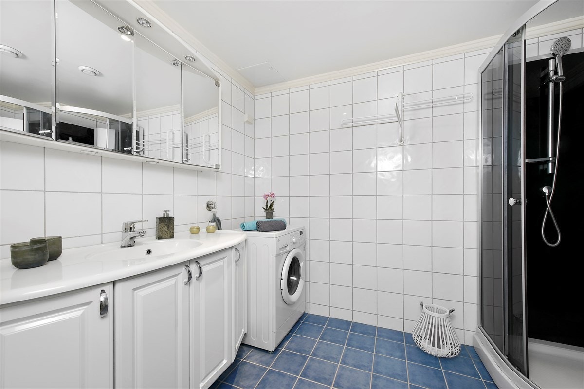 Badet har blå fliser på gulv med gulvvarme, hvite fliser på vegger og downlights i himling. Galleribilde