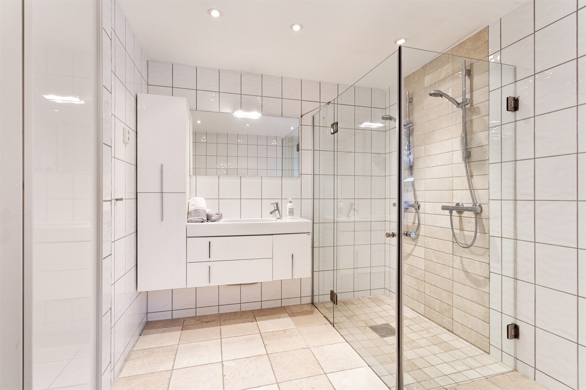 Badet inneholder dusjsone, vegghengt toalett, stor servant med underskap og speil Galleribilde