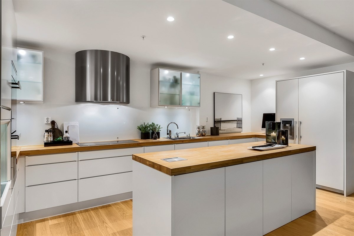 Kjøkkeninnredning i stilrent design med integrerte hvitevarer i form av induksjonstopp, stekeovn, mikroovn, oppvaskmaskin, samt side-by-side kjøleskap med isbitmaskin. Innredningen har god lagringsplass, kjøkkenøy og nisje for "kaffebar". Galleribilde