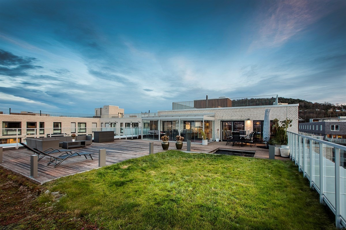 Terrassen på 153 kvm er vakkert opparbeidet med stor platting og belysning, og en liten hageflekk tilbyr gress og sedum under føttene. Her oppe på taket kan man trekke seg tilbake i lune omgivelser innenfor vinterhagens glassfasade, eller nyte solen ute p Galleribilde