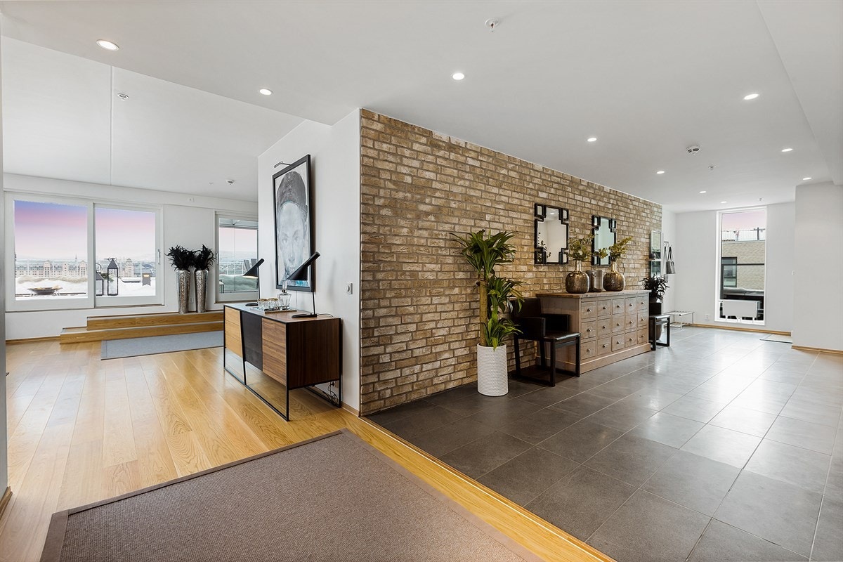 Heisen tar deg direkte opp til leilighetsplan, og vel innfor dørstokken venter toppleilighetens romslige hall. Rommet har blanke gulvfliser, hvitmalte overflater med innslag av forblendingsstein, og downlights i himling. Galleribilde