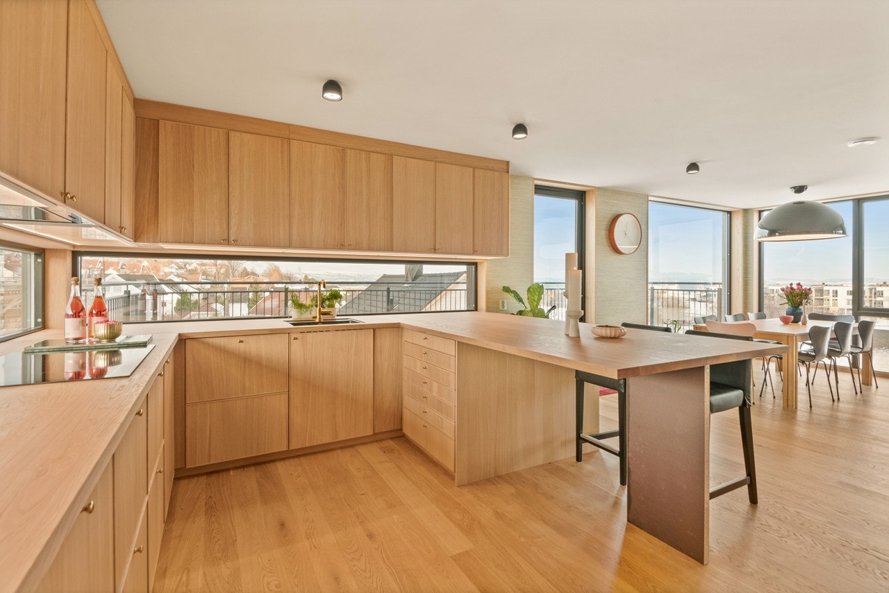 Skapene har trefargede, glatte fronter og over benken er det et langsgående vindu som gir en lys og herlig arbeidsplass. Videre har kjøkkenet integrert oppvaskmaskin, stekeovn, platetopp, kjøle-/fryseskap og mikrobølgeovn. Galleribilde