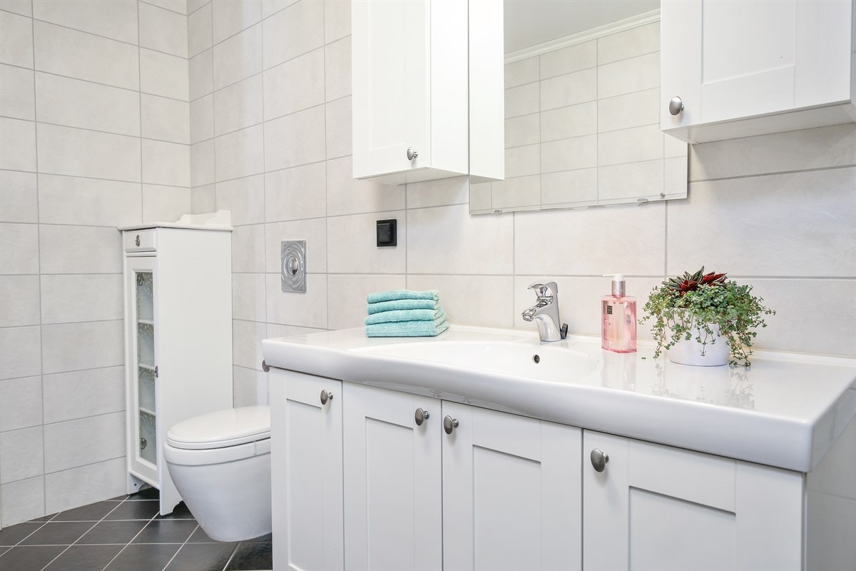 Badet nærmest ytterdøren har grå fliser på gulv med gulvvarme og lyse fliser på veggene. Galleribilde