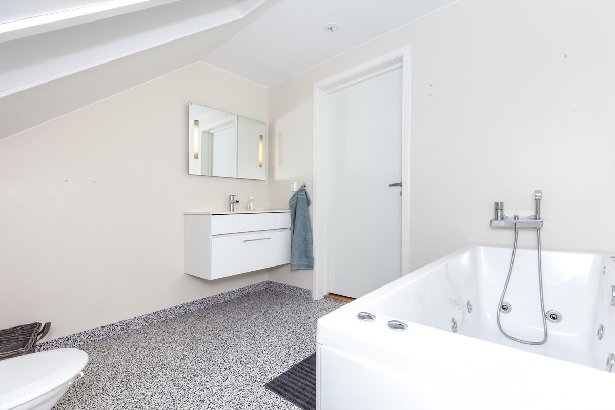 Badet i boligens annen etasje har lysmalte overflater og belegg på gulv med varmekabler. Innredningen består av moderne servantmøblement, speil med LED belysning, toalett og frittstående massasjekar. Galleribilde