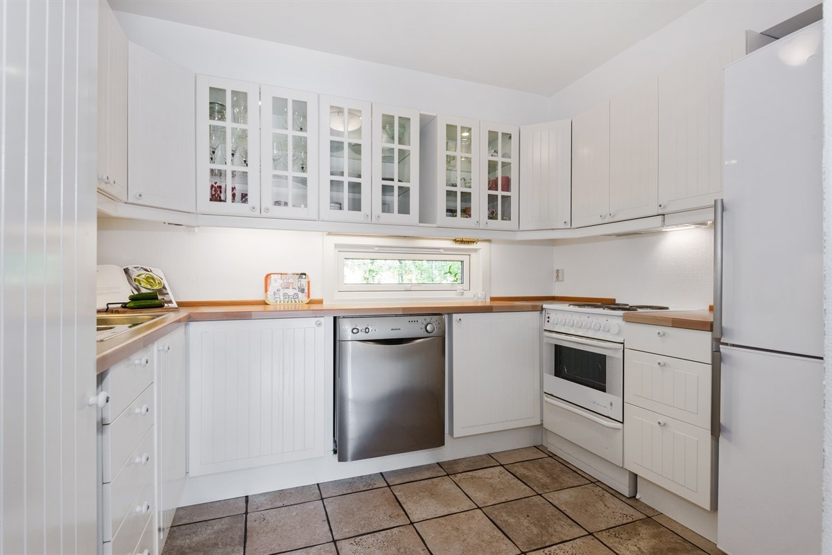 IKEA-kjøkken (2006) med lyse fronter og fliser over benk. Enkelte overskap med vitrinefronter gir et mykere inntrykk Galleribilde