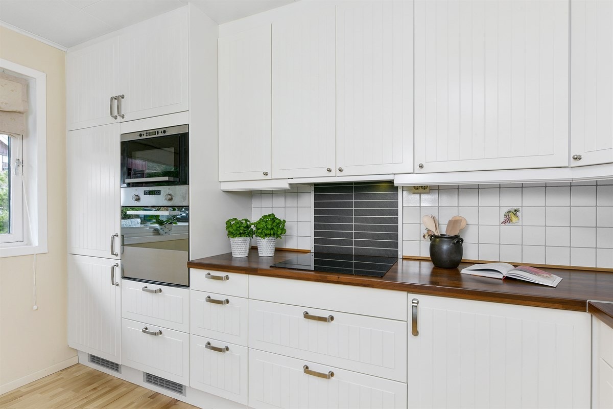 Innredningen er fra Ikea, fra 2009, og har hvite, profilerte fronter, vitrineskap og en laminert benkeplate med nedfelt oppvaskkum. Galleribilde
