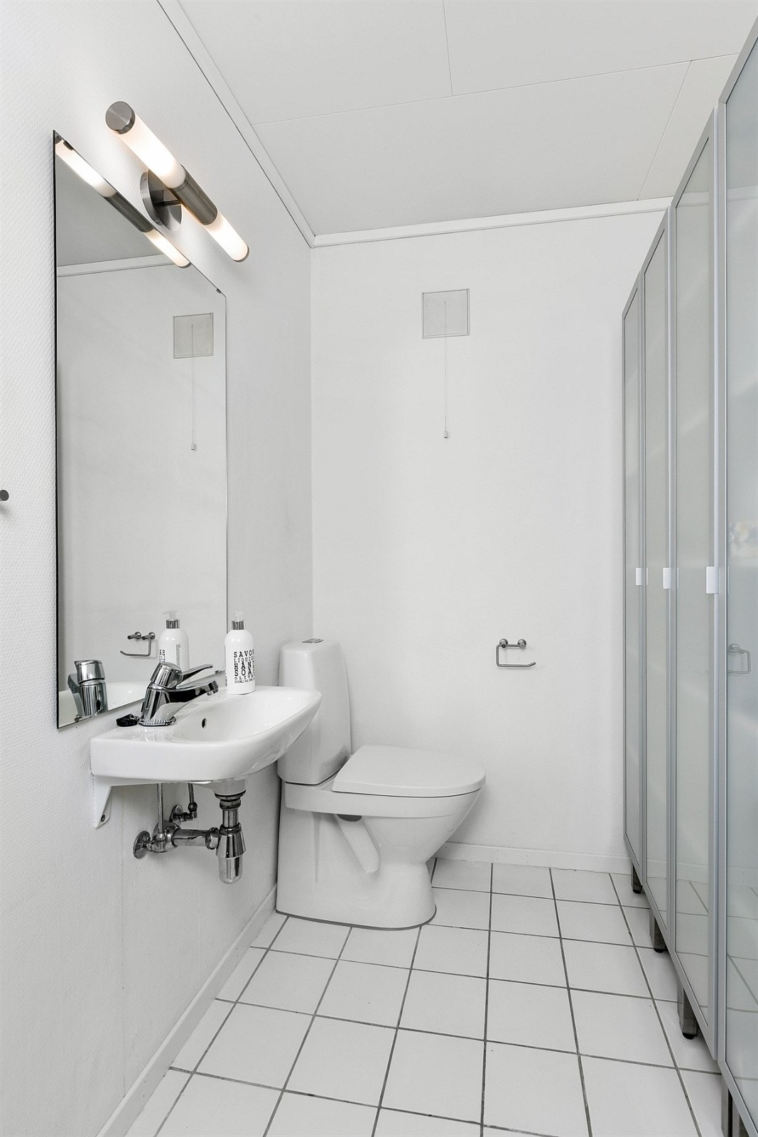 Det kombinerte badet/vaskerommet ligger i underetasjen og har grå fliser på gulv og lysmalte panelvegger. Galleribilde