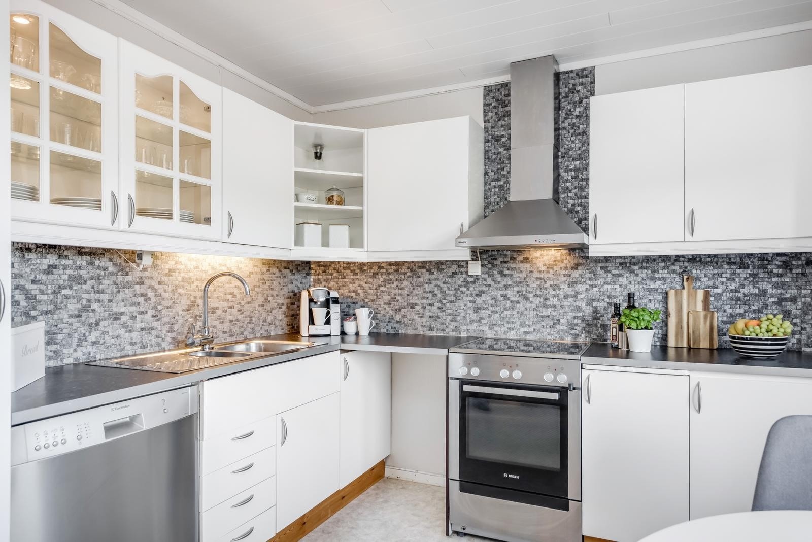 Kjøkkenet ligger adskilt fra stuen og har en elegant kjøkkeninnredning med lyse fronter og grå benkeplate med nedfelt oppvaskkum. I tillegg er det fine, klassiske detaljer som vitrineskap og åpne hyller. Galleribilde