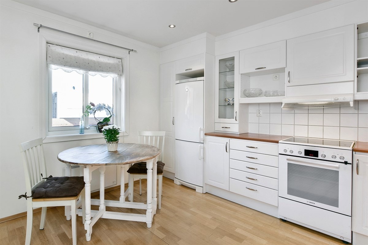 Innredningen har hvite profilerte fronter, hyller, vitrineskap og laminert benkeplate med dobbel oppvaskkum. Galleribilde