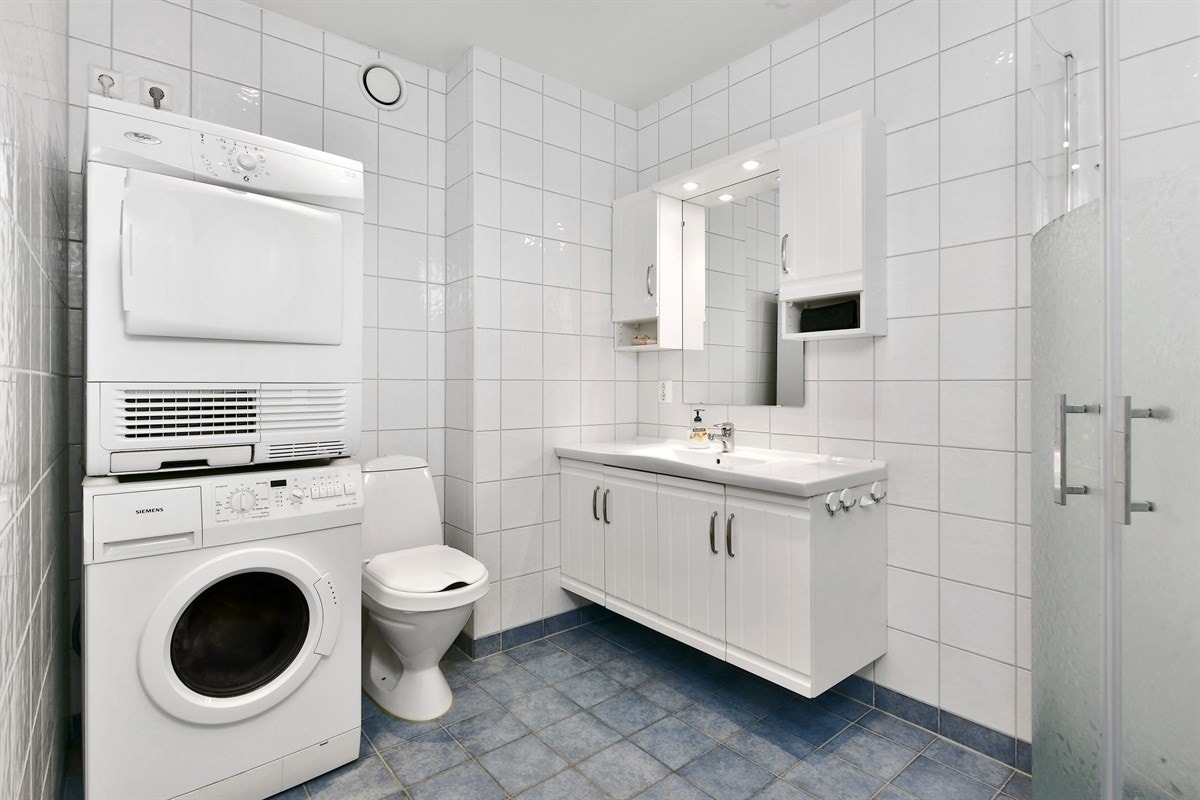 Leiligheten inneholder et romslig bad med listefritt tak. Rommet har blå fliser på gulv, gulvvarme og hvite fliser på veggene. Galleribilde