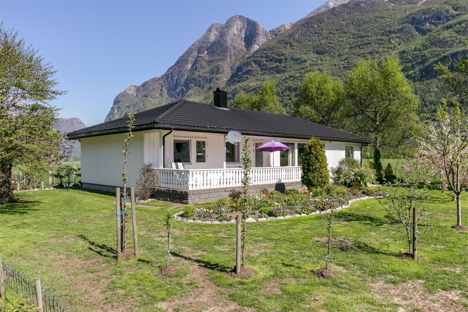 Bustaden er omkransa av ein frodig hage med frukttre, blomsterbed, prydbusker og anna beplanting Galleribilde