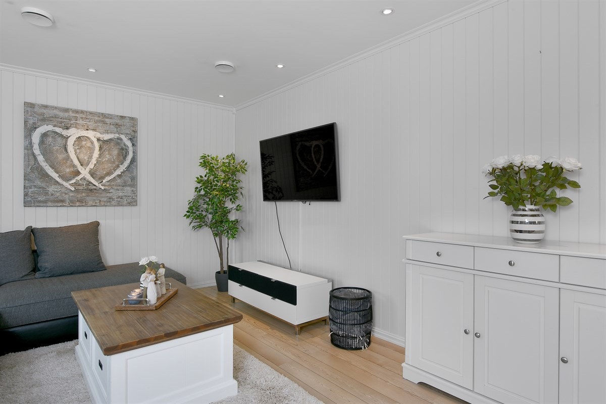 Rommets avlange utforming gir fin plass til sofaløsning med tilhørende tv-møblement og utenfor kjøkkenet er det god plass til langbord for sosiale sammenkomster. Galleribilde